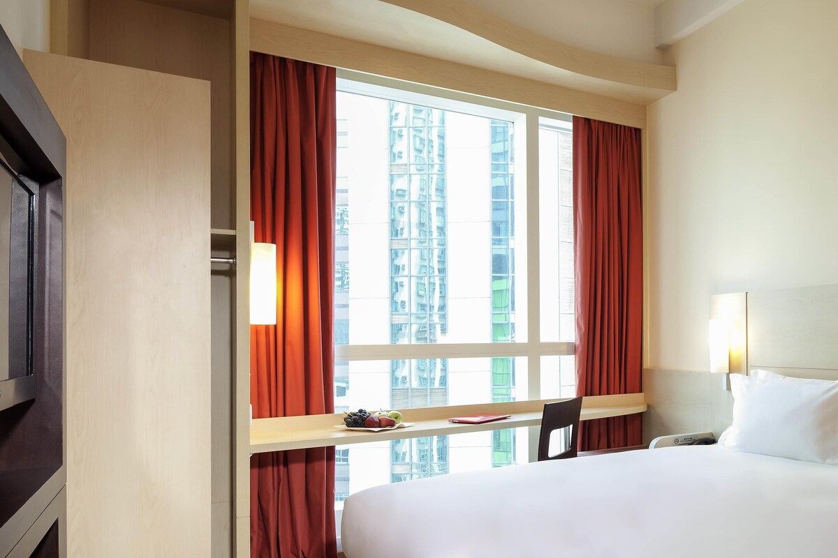 A hotel room with a bed, a desk, a chair, a TV, and a window with curtains.