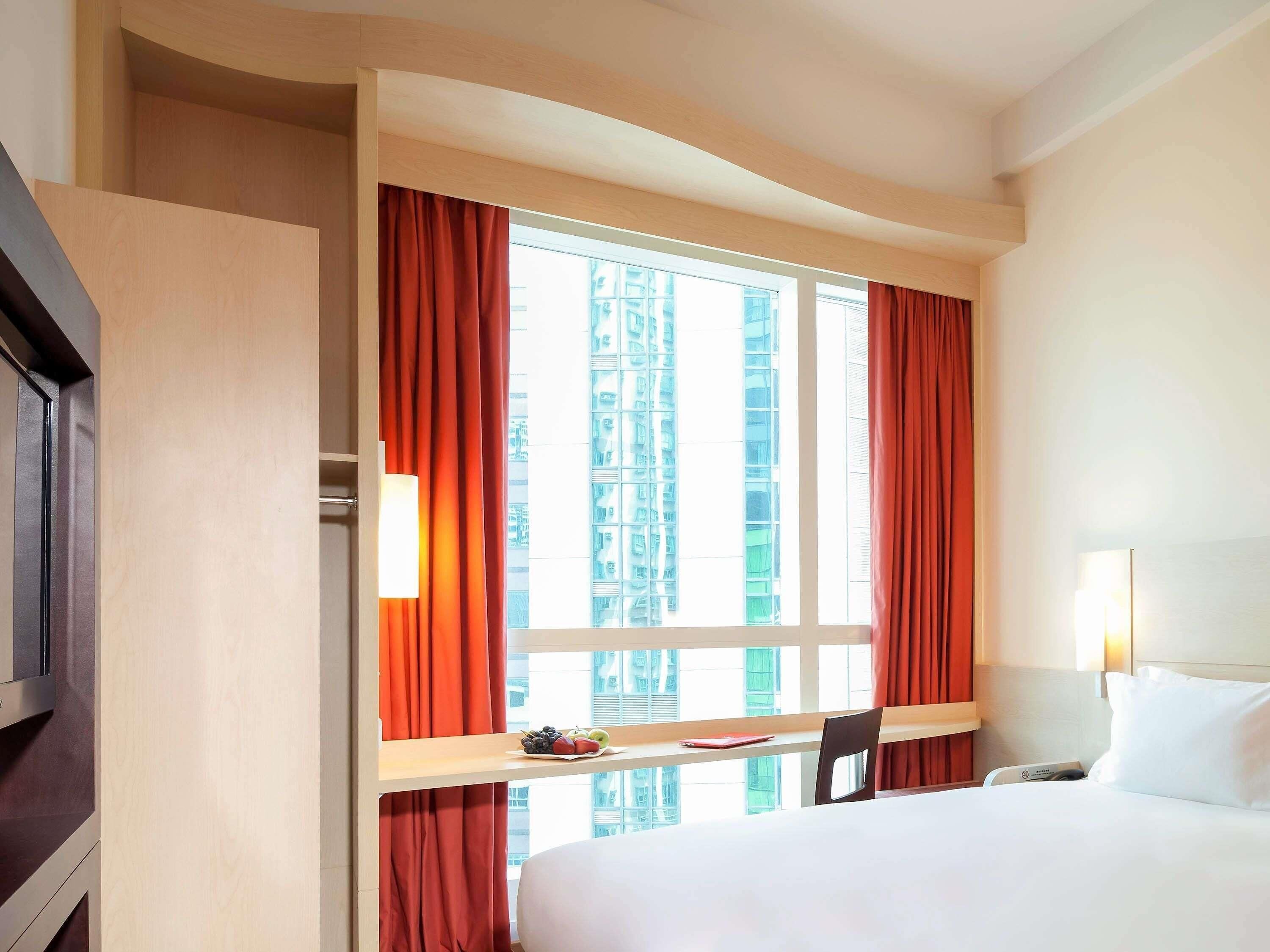 Une chambre d’hôtel avec un lit, un bureau et une chaise, une télévision et une fenêtre avec des rideaux.