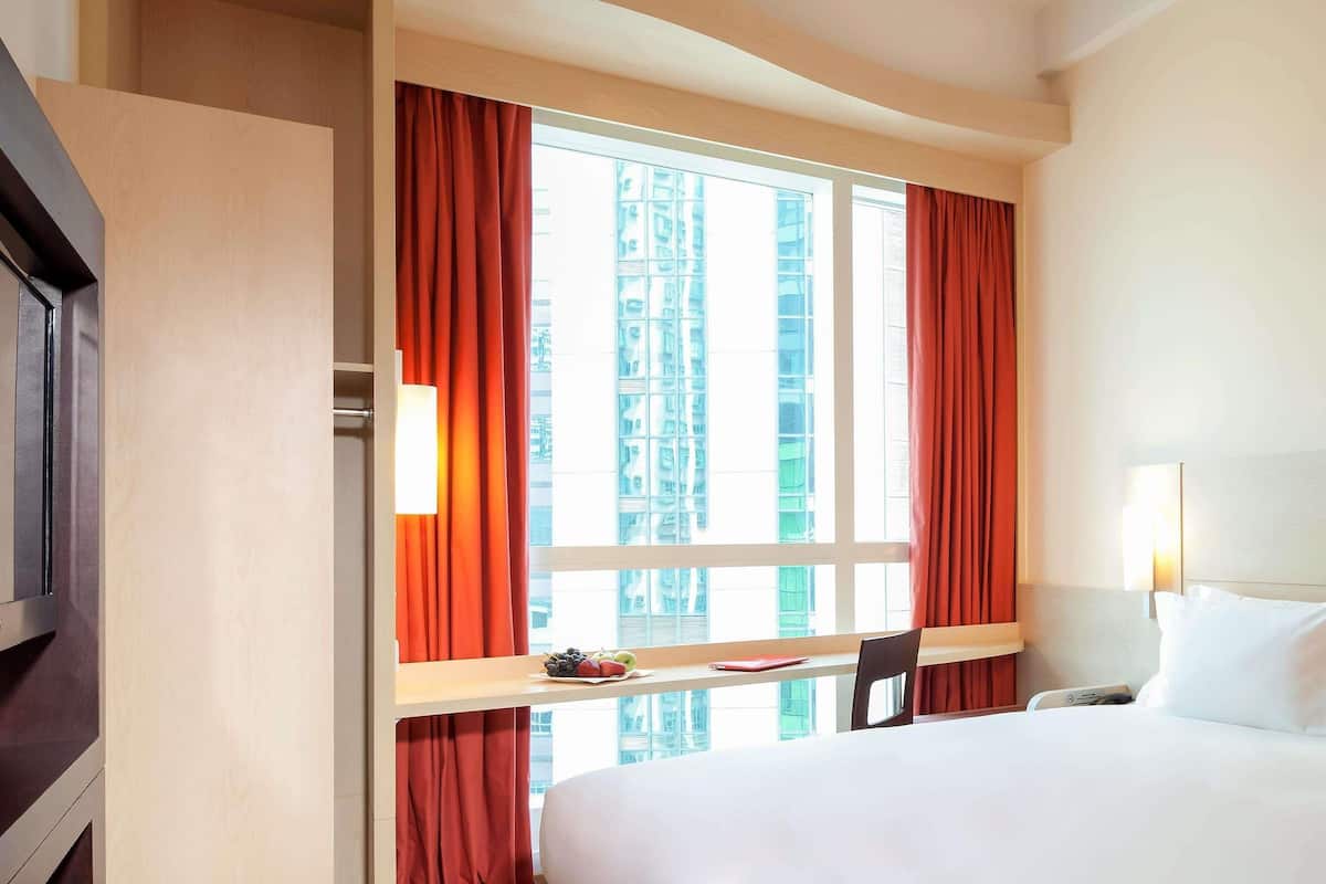 Una habitación de hotel con cama, escritorio con silla, televisor y ventana con cortinas.