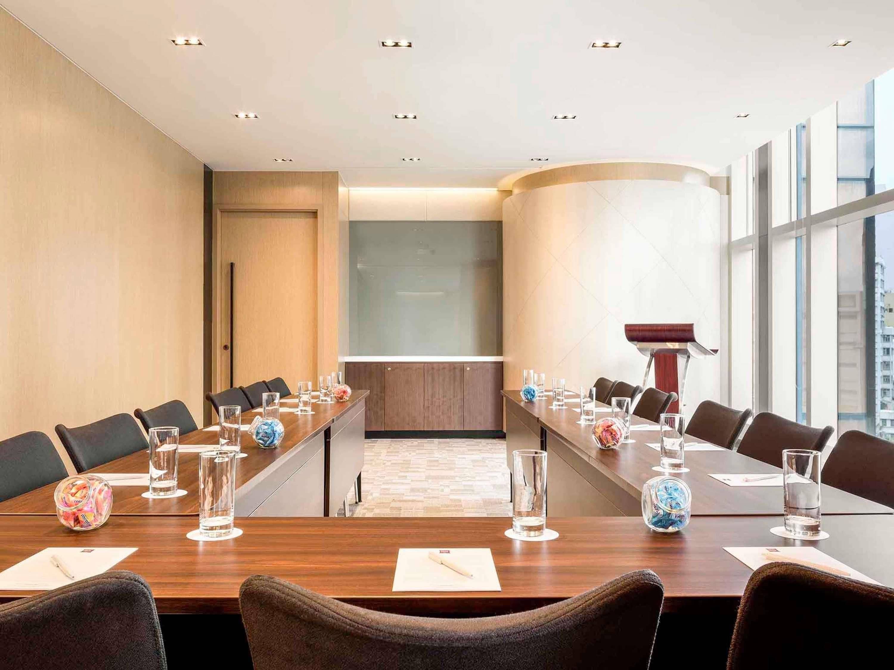 Een vergaderzaal met een lange tafel, stoelen en een spreekgestalte.
