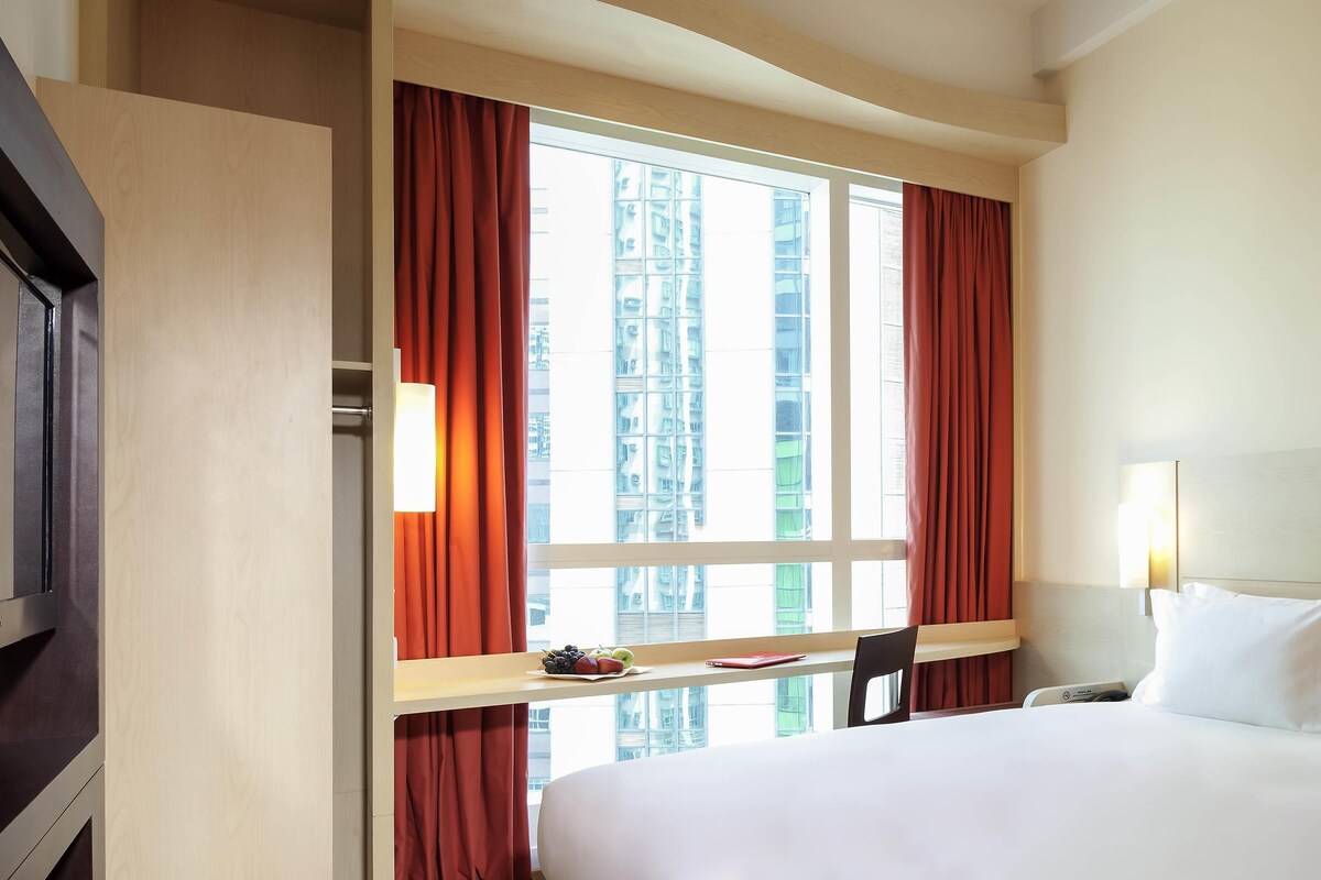 A hotel room with a bed, a desk, a chair, a TV, and a window with curtains.
