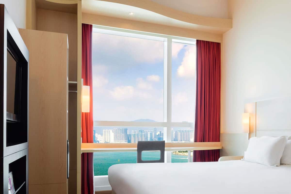 Habitación de hotel con cama, televisión, ventana con cortinas y vista a la ciudad.