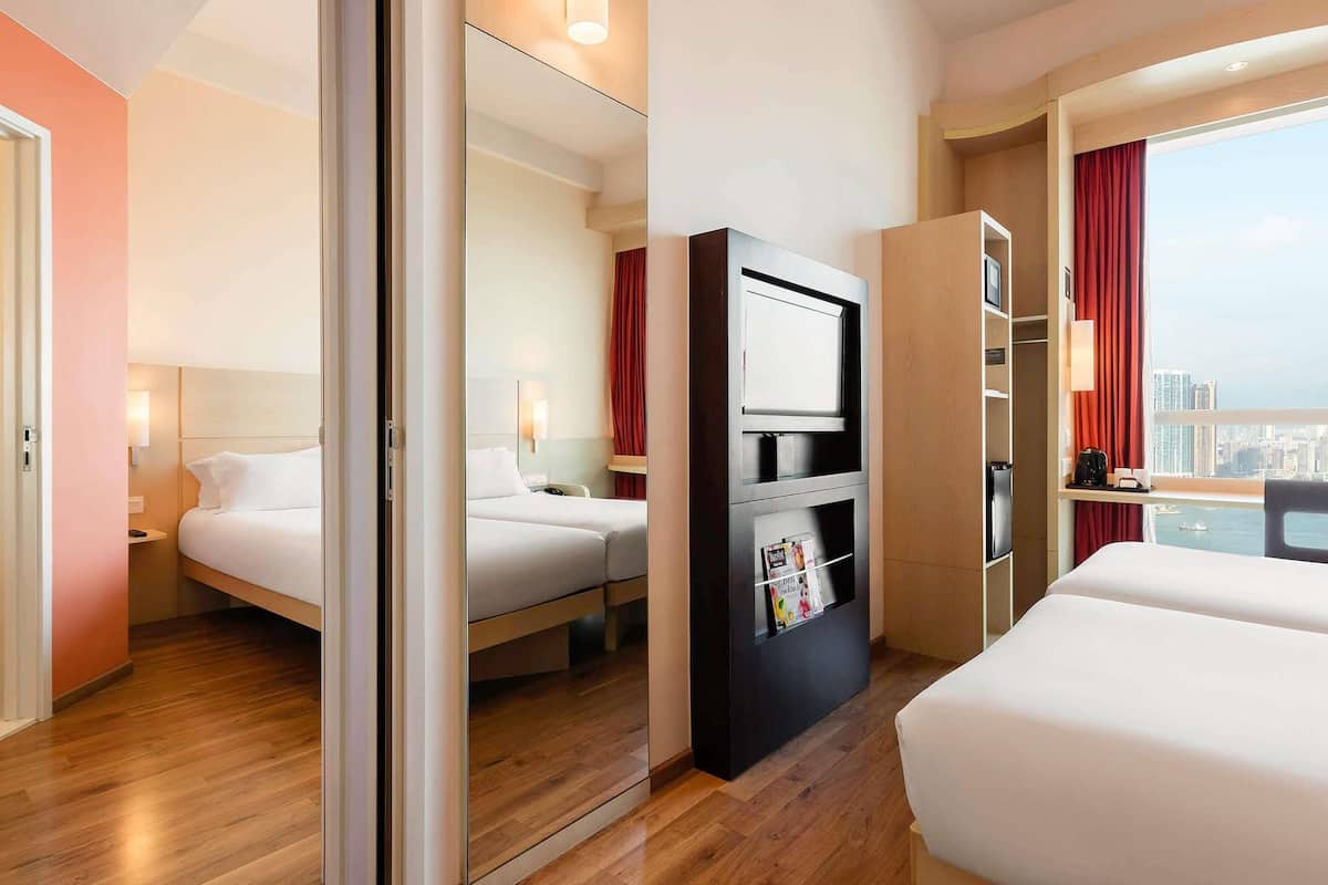 Habitación de hotel con dos camas, televisión, minibar y vista a la ciudad.