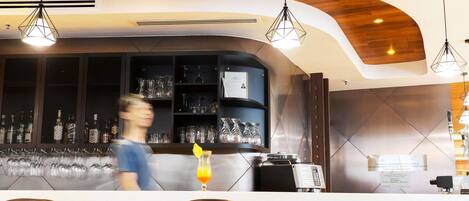 Uma área de bar com assentos, uma máquina de café e prateleiras com copos e garrafas.