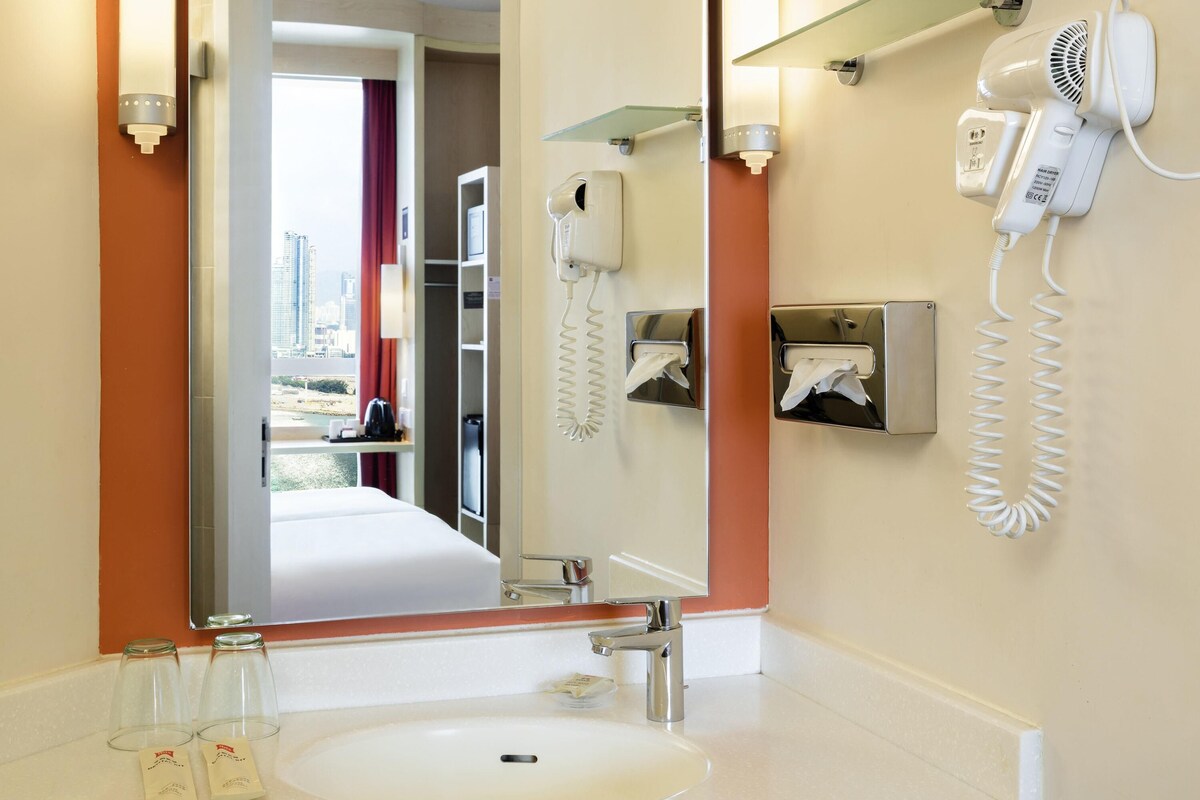 Een hotelbadkamer met een wastafel, spiegel, haardroger en handdoekdispenser.