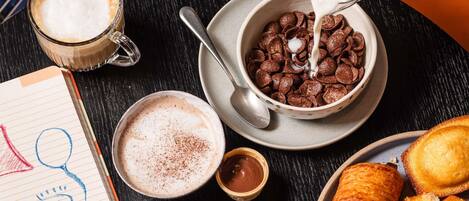 A breakfast setting with cereal, milk, coffee, croissants, and a drawing on a notepad.