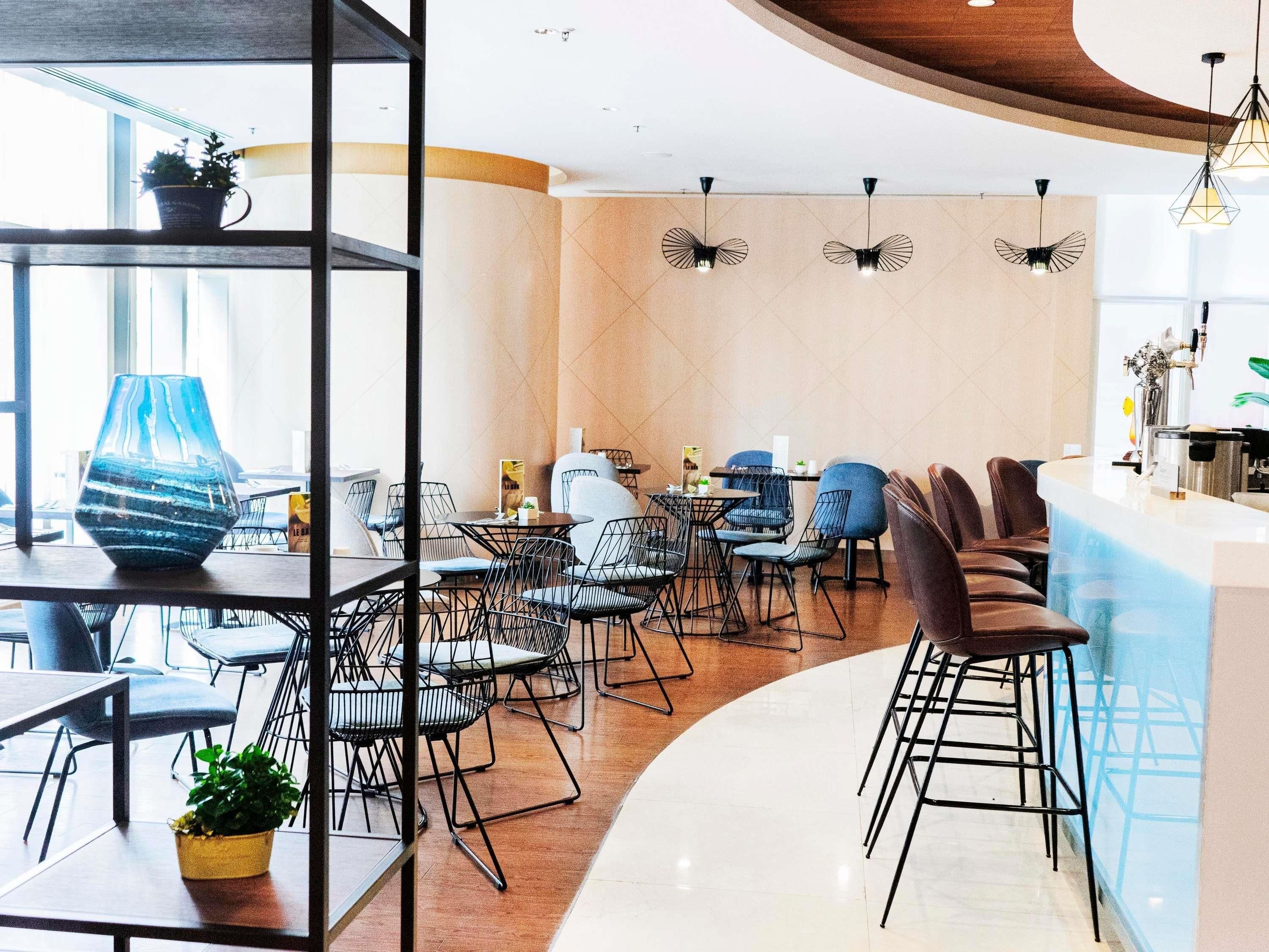 A modern dining area with a curved counter, black metal chairs, and a mix of round and square tables.