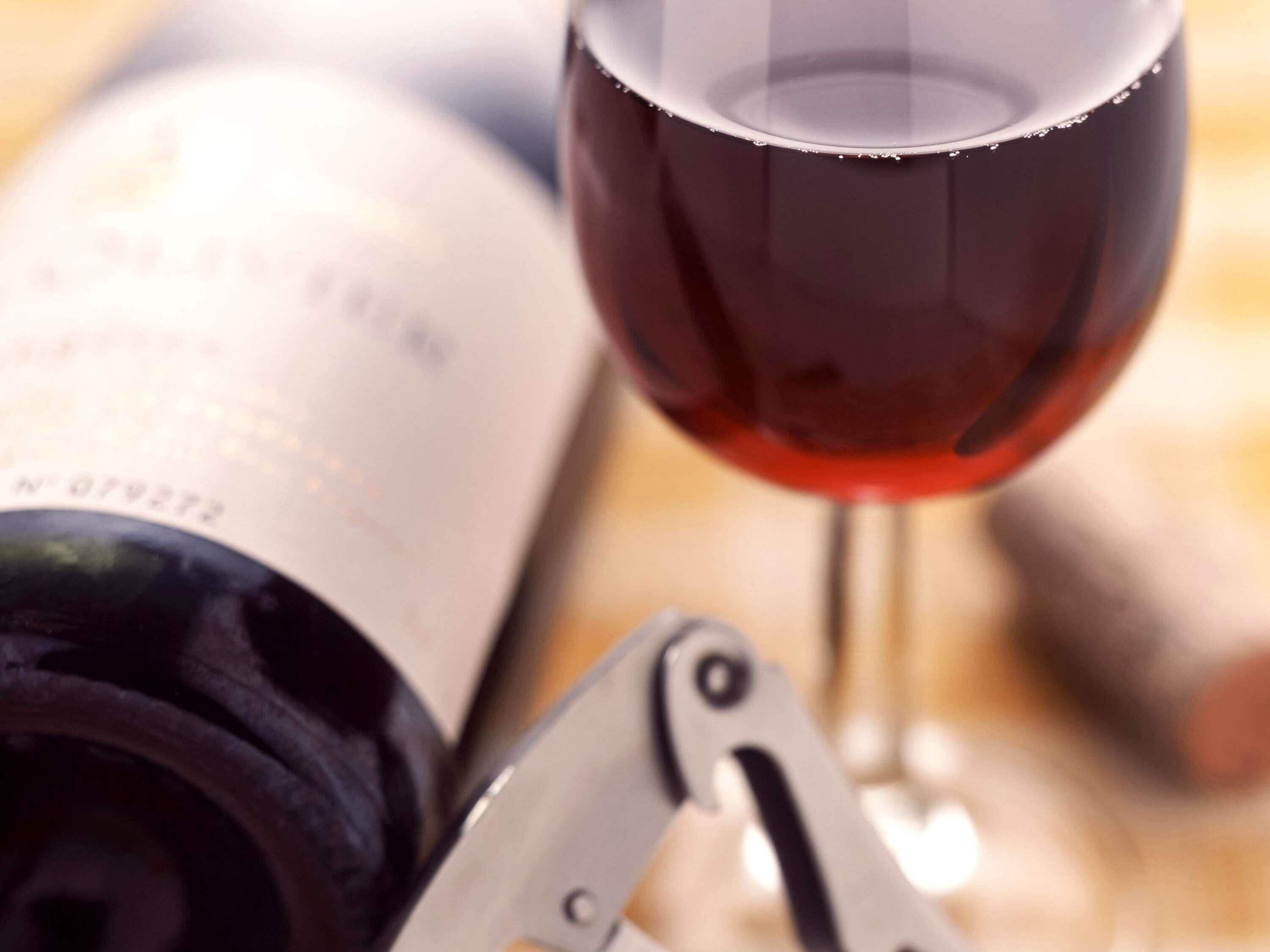 Una botella de vino y una copa con un sacacorchos.