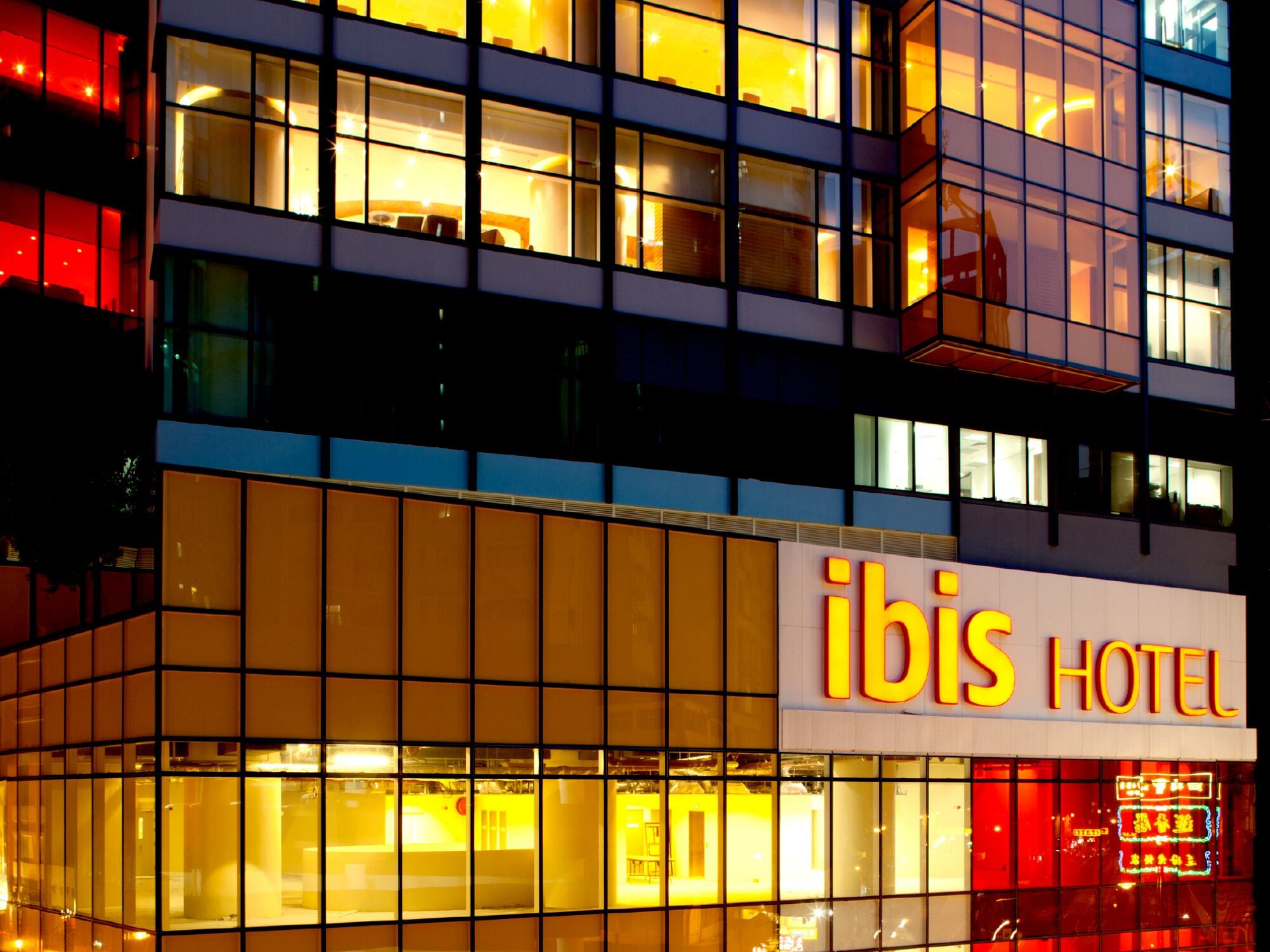 Un hôtel à l’architecture moderne, avec une façade dotée de grandes fenêtres et d’une enseigne « ibis HOTEL » bien visible.