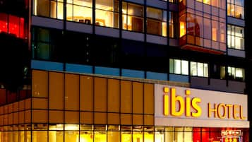 Un hôtel à l’architecture moderne, avec une façade dotée de grandes fenêtres et d’une enseigne « ibis HOTEL » bien visible.
