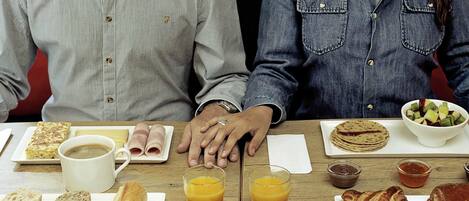 Mesa de café da manhã com pratos de comida, bebidas e um casal sentado.