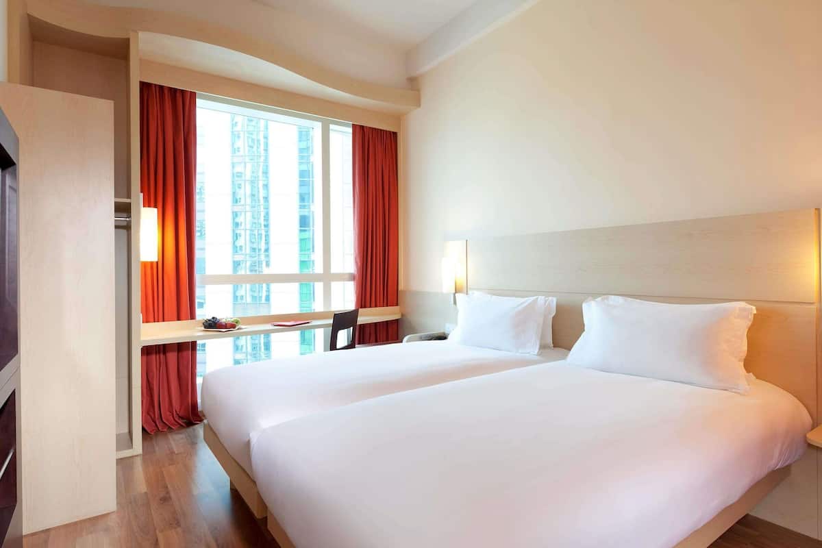 Habitación de hotel con una cama grande, un escritorio con silla, una ventana con cortinas y vista a la ciudad.