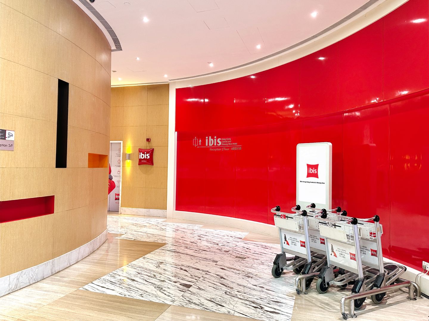 A hotel lobby with a red and beige color scheme, a reception desk, and a luggage cart.