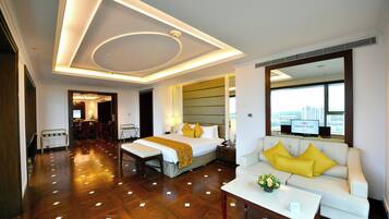 A hotel room with a bed, a sofa, a dining area, and a view of the city.