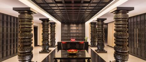 A long, narrow hotel lobby with a central seating area, flanked by tall, ornate columns.
