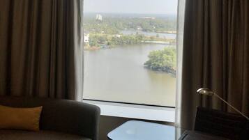 A hotel room with a large window, a sofa, a glass table, and a lamp.