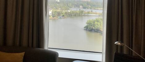 A hotel room with a large window, a sofa, a glass table, and a lamp.