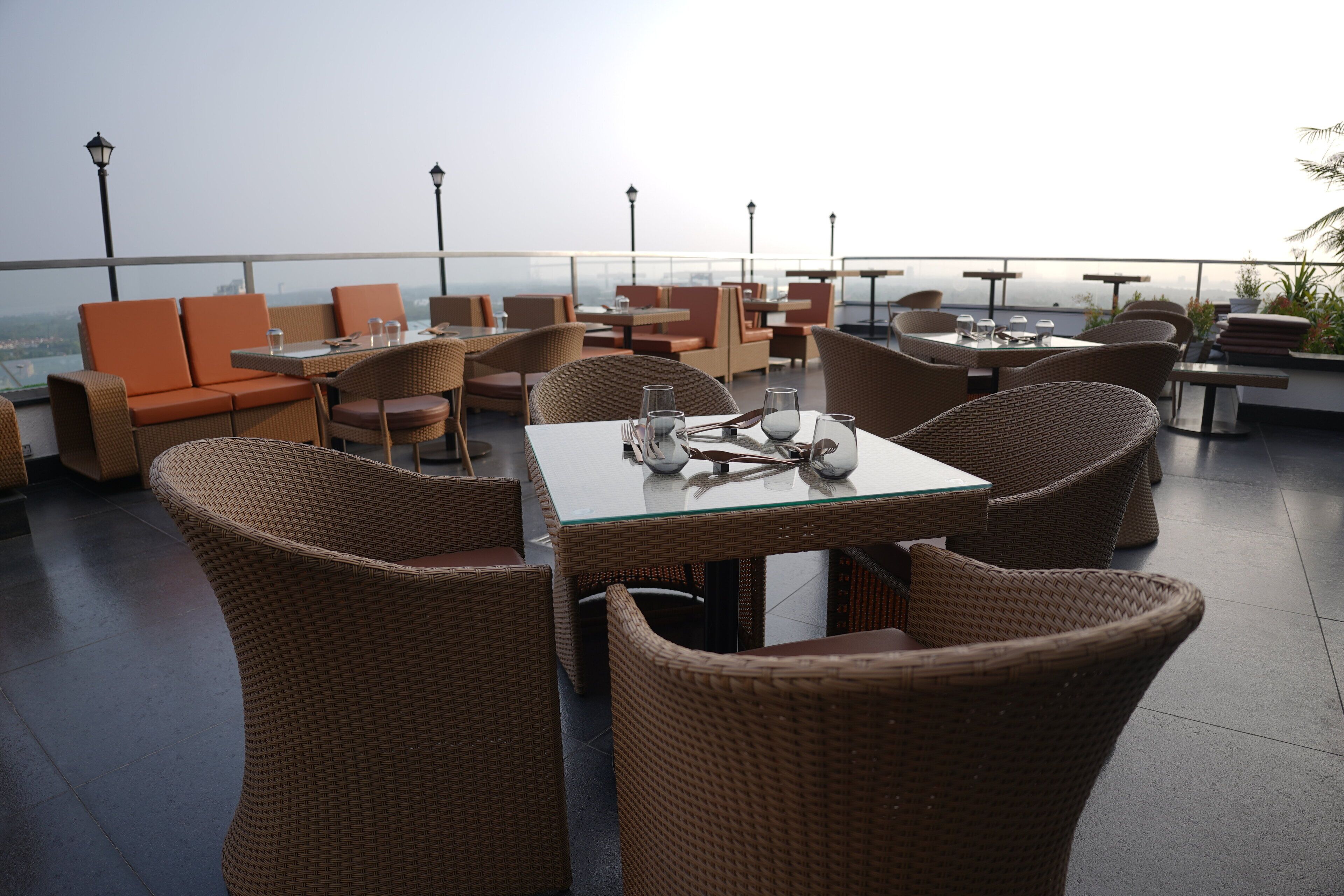 Un ristorante sul tetto con mobili in vimini e tavoli in vetro, che offre vista sulla città.