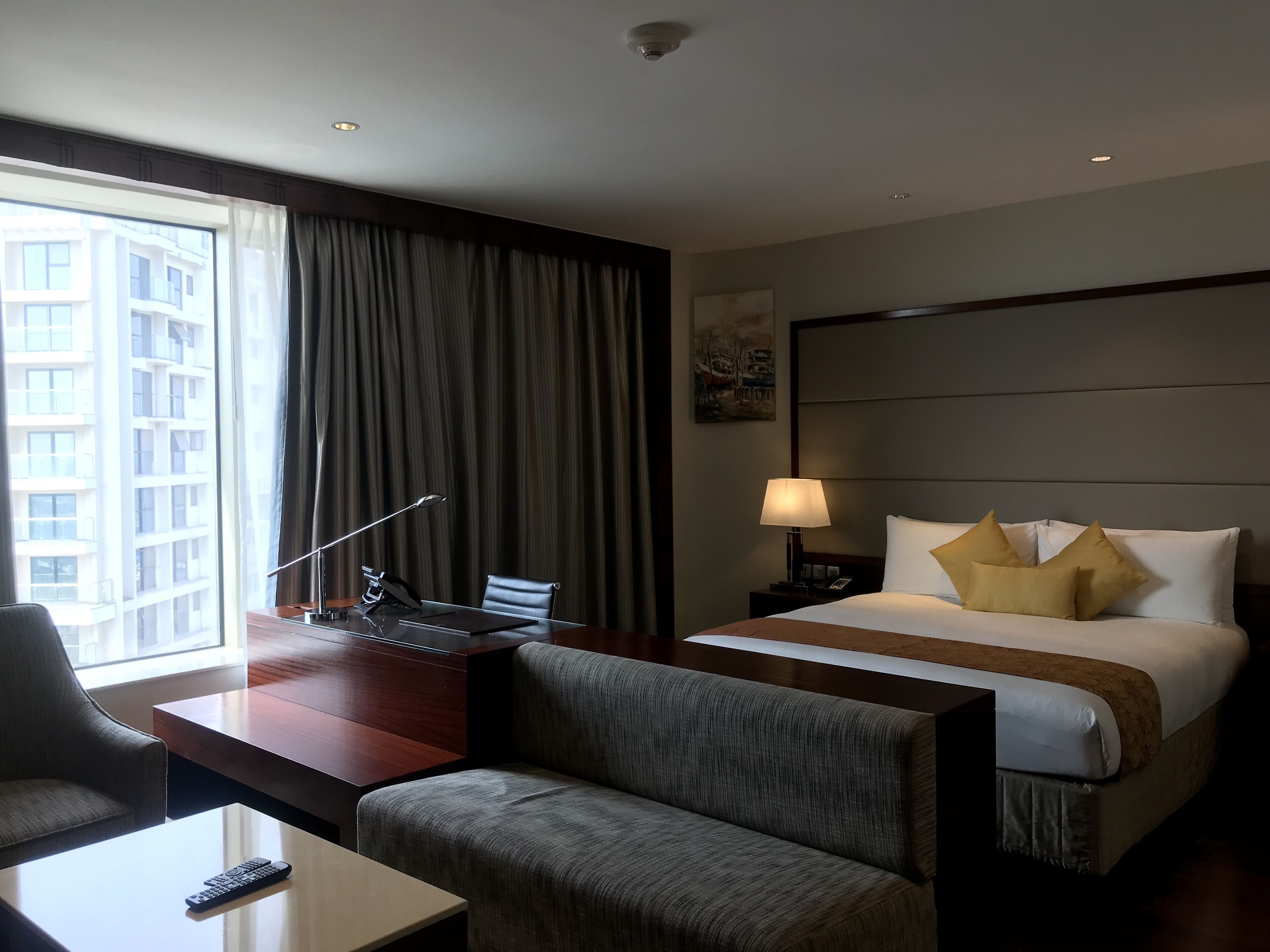 Een hotelkamer met een bureau, stoel, bed en uitzicht op een stadsbeeld door het raam.