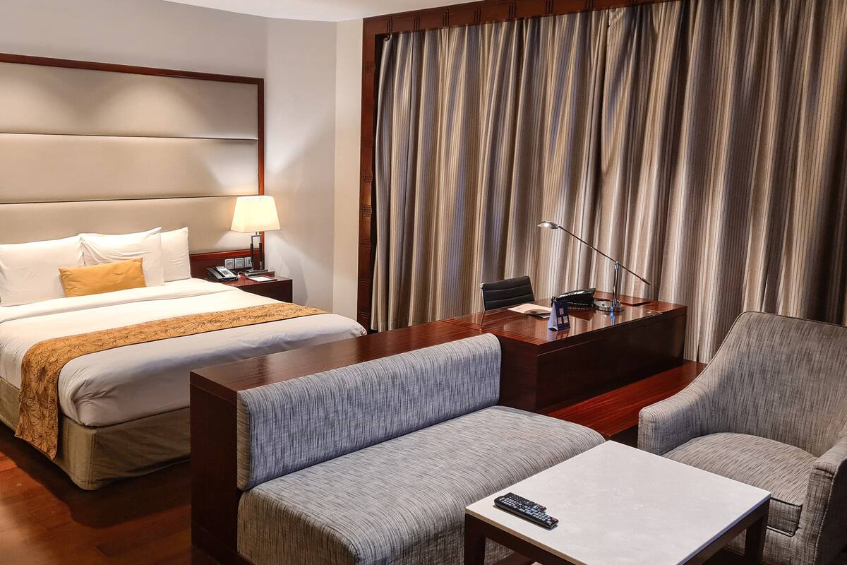 A hotel room with a large bed, two bedside lamps, a desk with a computer, a chair, and a TV.