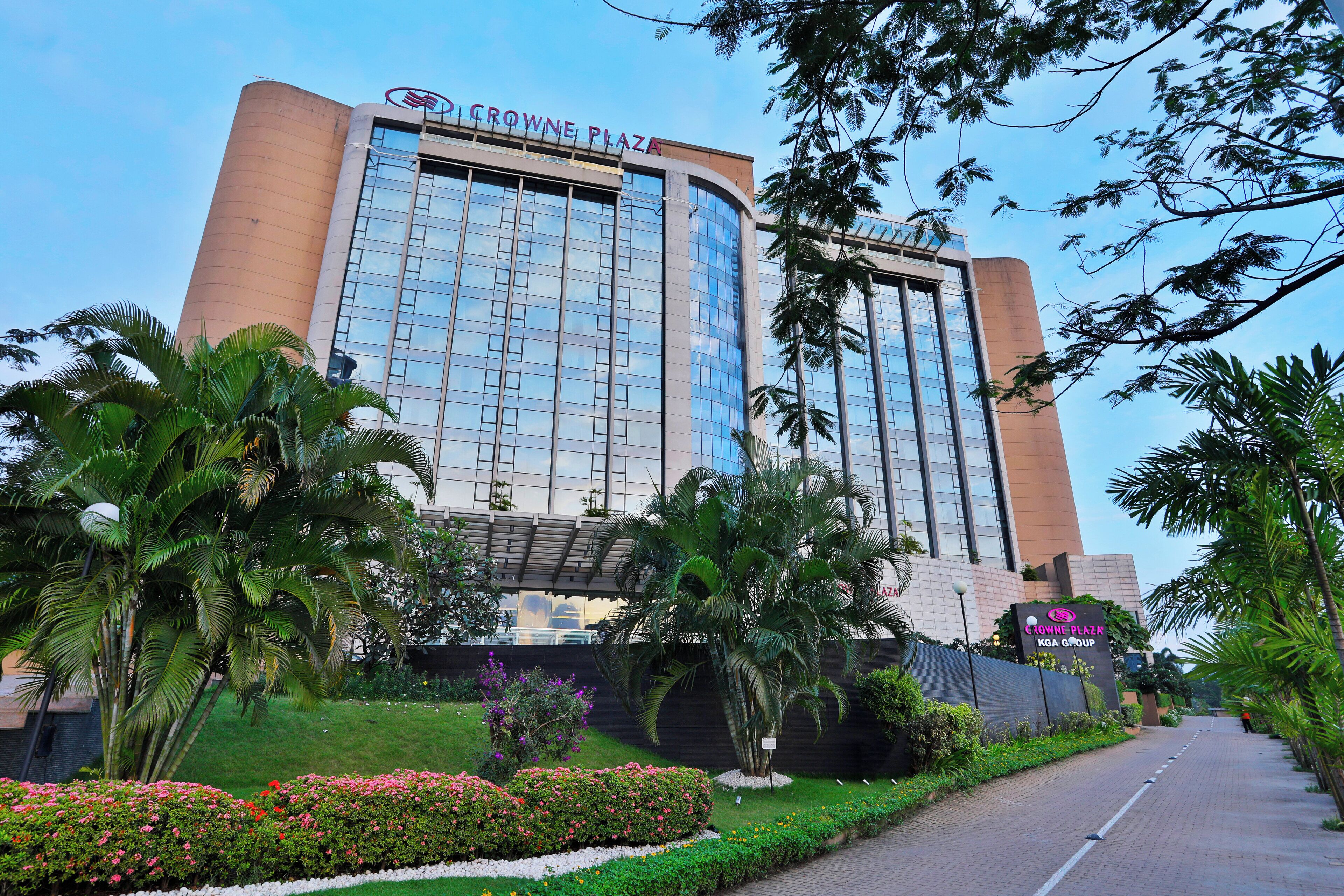 A modern hotel building with a glass facade, surrounded by lush greenery and a paved walkway.