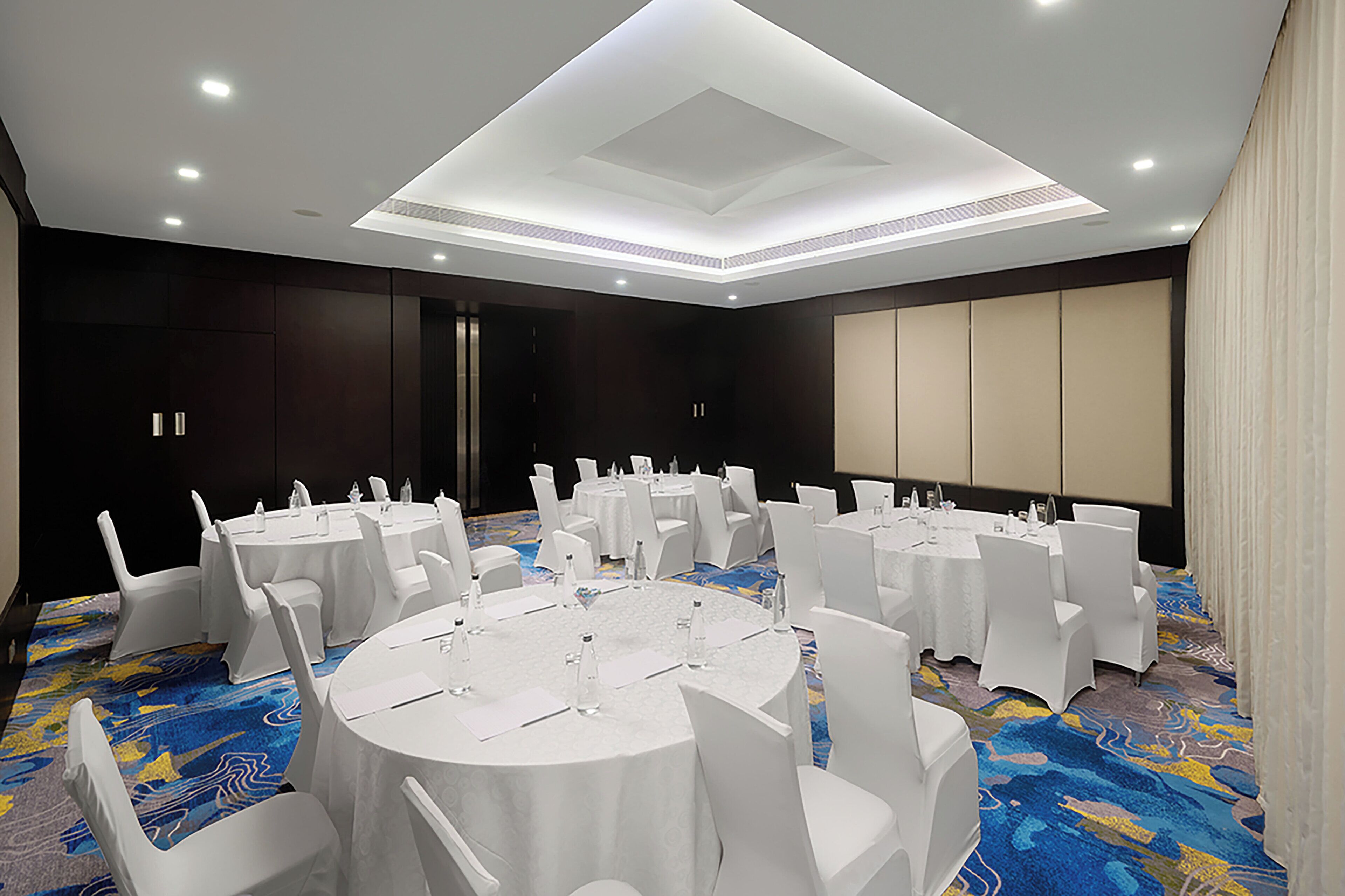 A conference room with round tables, white chairs, and a carpeted floor.