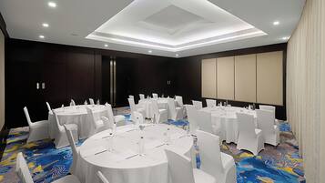 Una sala de conferencias con mesas redondas, sillas blancas y piso alfombrado.