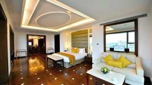 A hotel room with a large bed, a sofa, a dining area, and a view of the city. - Crowne Plaza Kochi by IHG (Kanayannur)