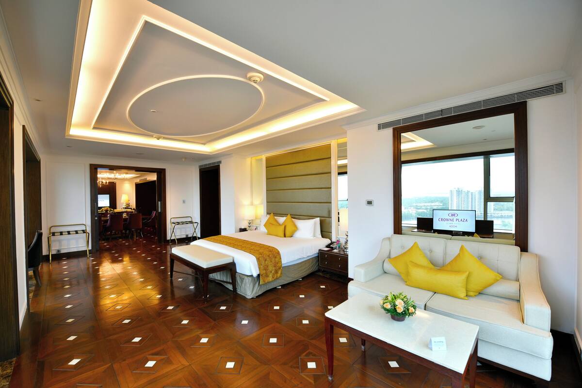 A hotel room with a large bed, a sofa, a dining area, and a view of the city.