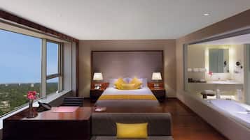 A modern hotel room with a large bed, a desk, a sofa, a view of the city, and a bathroom with a large mirror.
