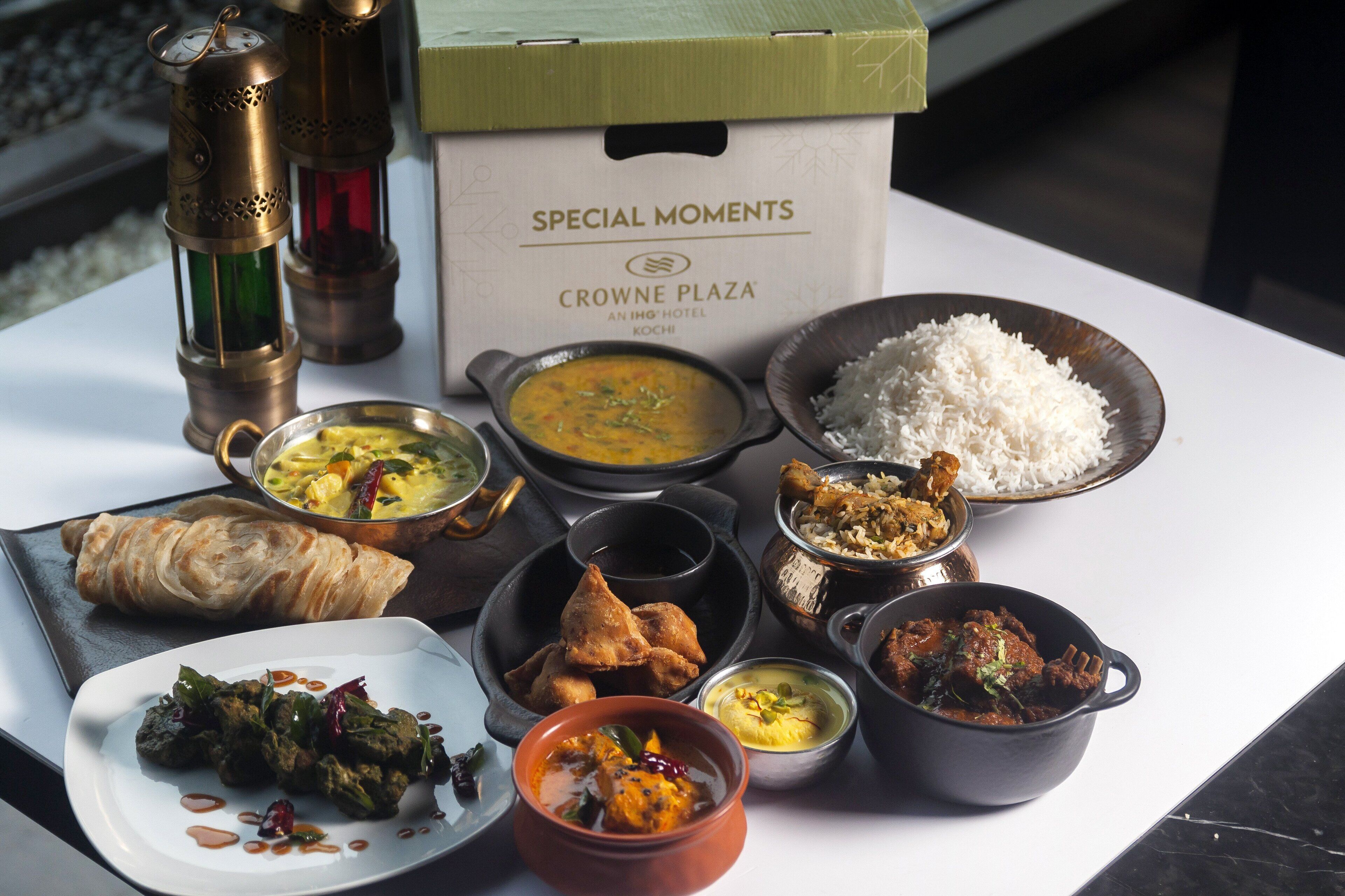 A variety of dishes on a table, including rice, curry, and samosas, with a box labeled "SPECIAL MOMENTS CROWNE PLAZA".