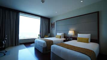 A hotel room with two beds, a desk, a chair, and a large window.
