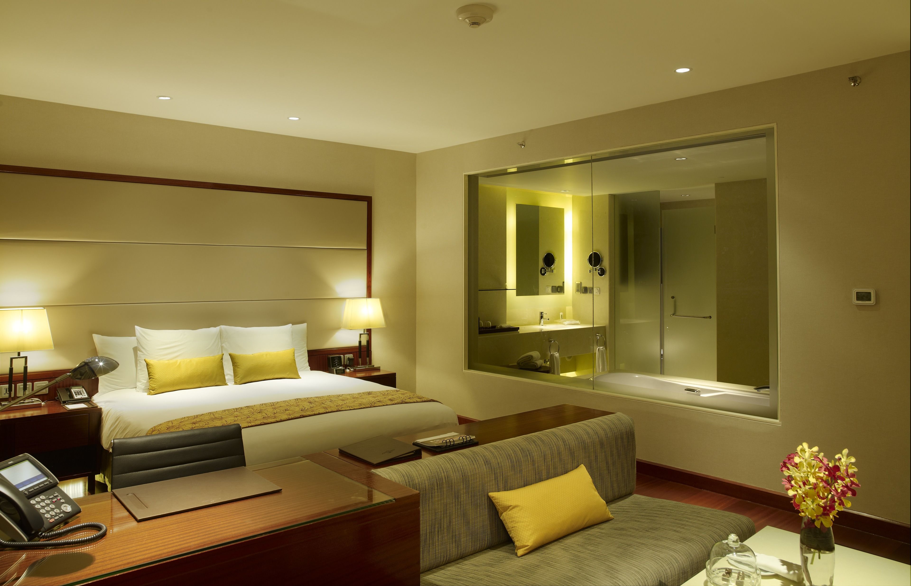 Habitación de hotel con una cama grande, lámparas de noche, un escritorio con teléfono, un sofá y un espejo amplio.