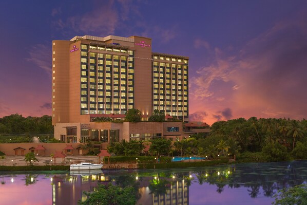 A high-rise hotel with multiple floors, a swimming pool, and a dock with a boat. - Crowne Plaza Kochi by IHG (Kanayannur)
