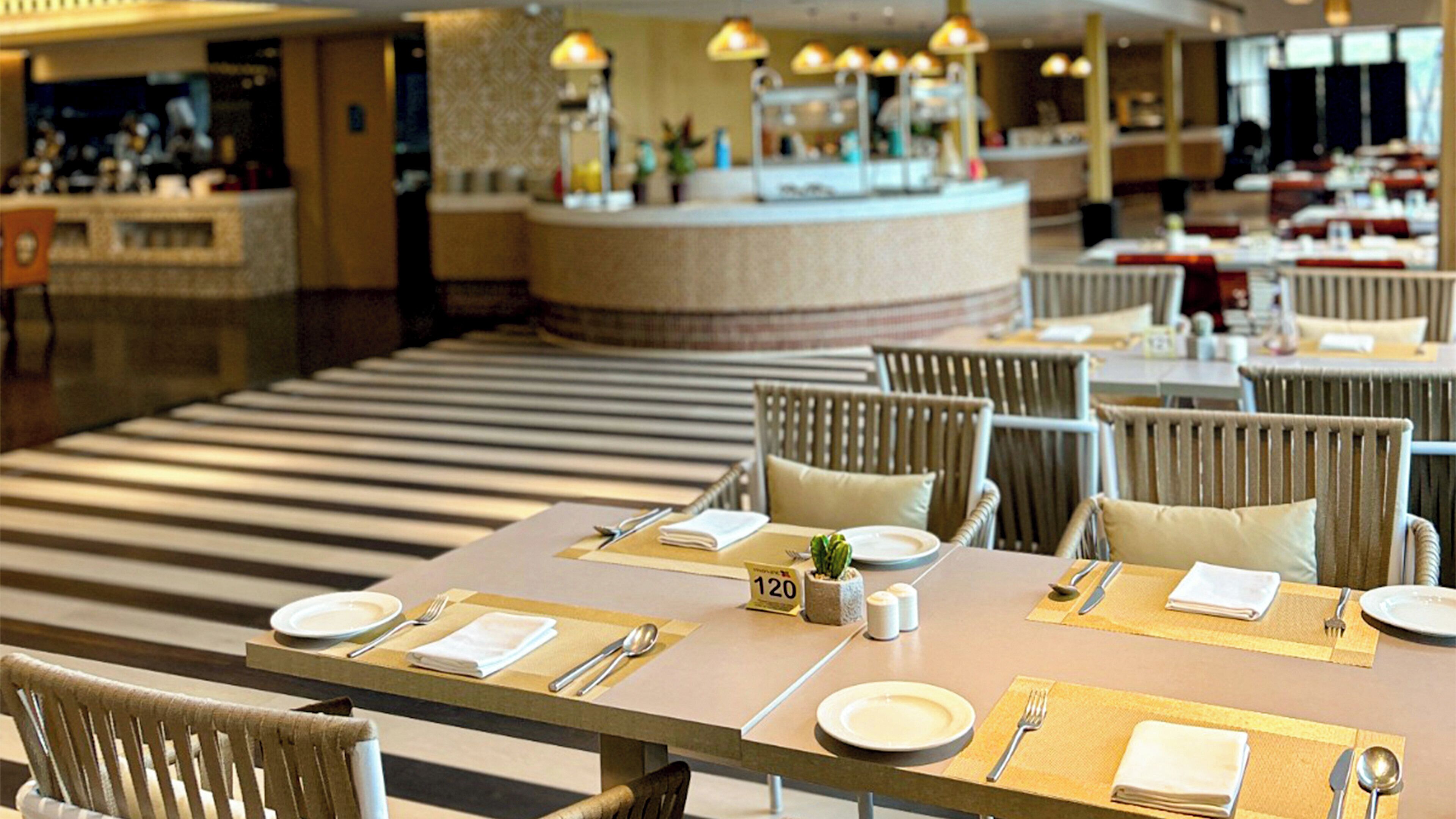 A hotel dining area with tables set for two, numbered placemats, and a counter in the background.