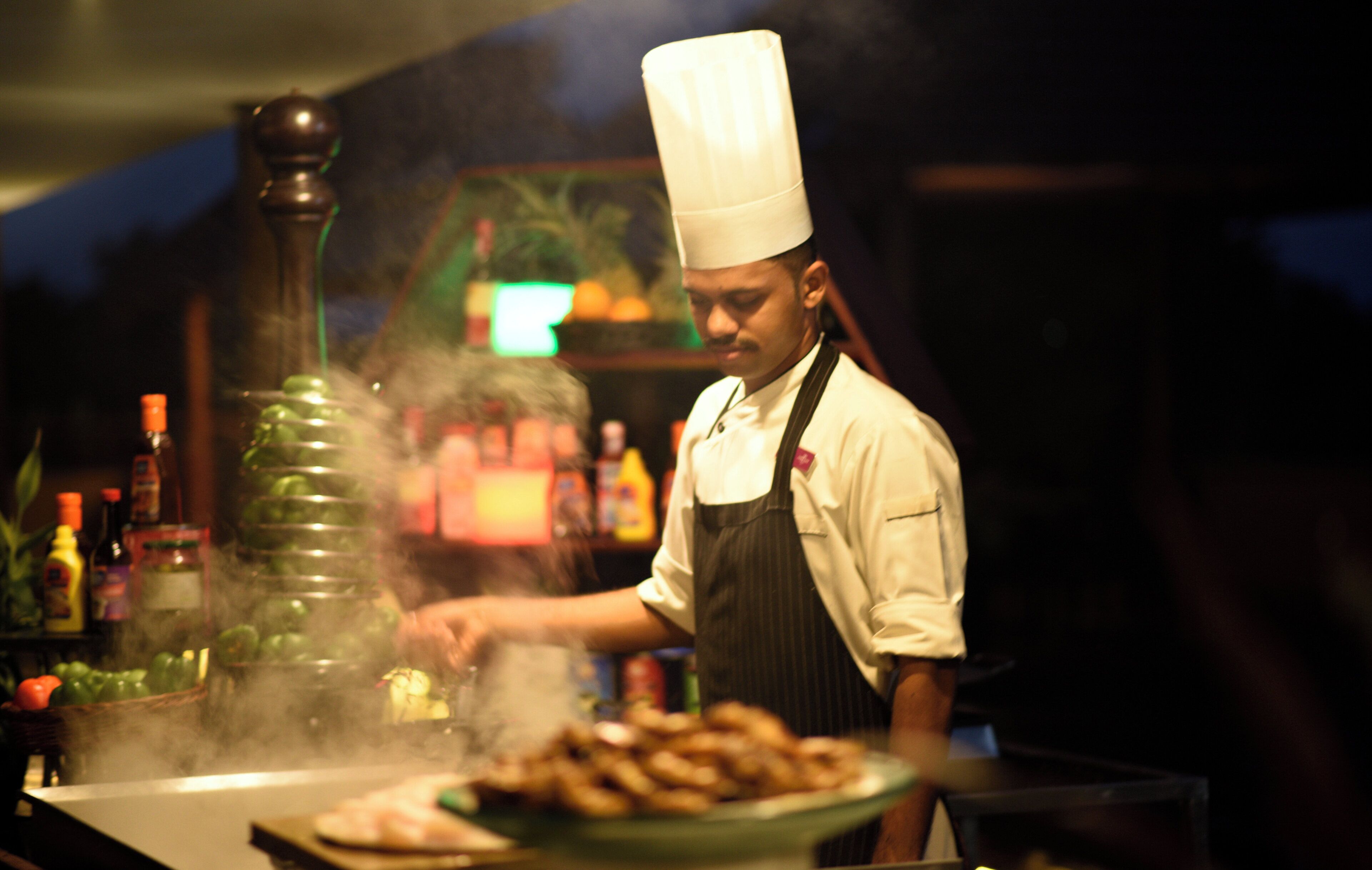A chef in a professional kitchen with a stove, cooking utensils, and a variety of ingredients.