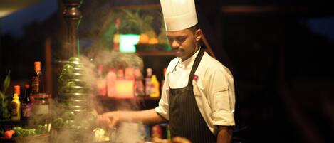 A chef in a professional kitchen with a stove, cooking utensils, and a variety of ingredients.