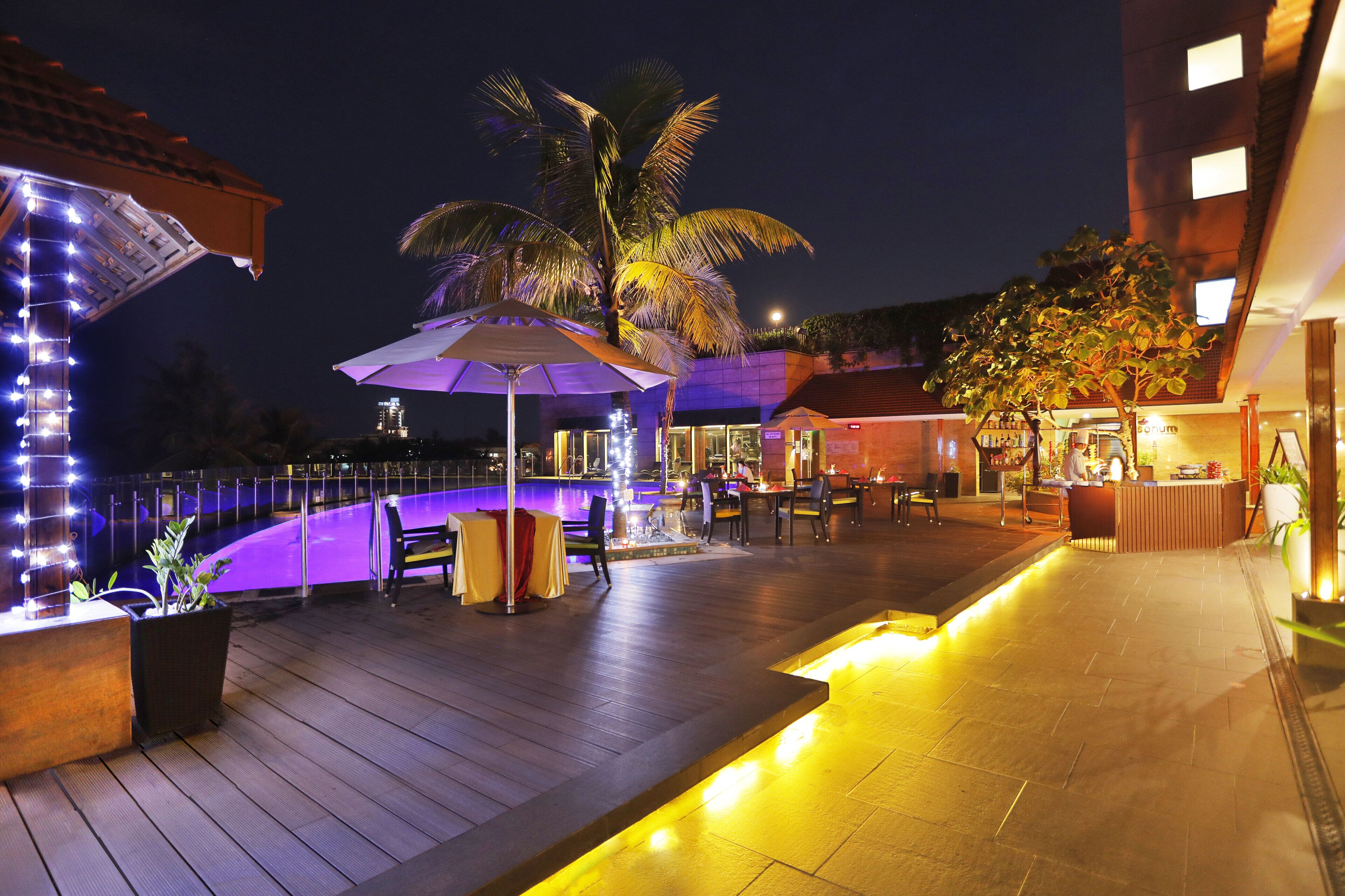 A nighttime outdoor area with a pool, umbrellas, and seating.