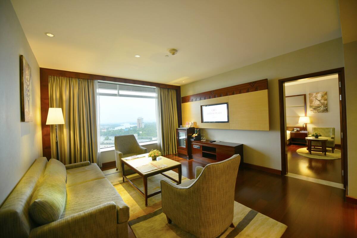A hotel room with a sofa, armchair, and a desk with a television.