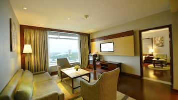 A hotel room with a sofa, armchair, and a desk with a television.