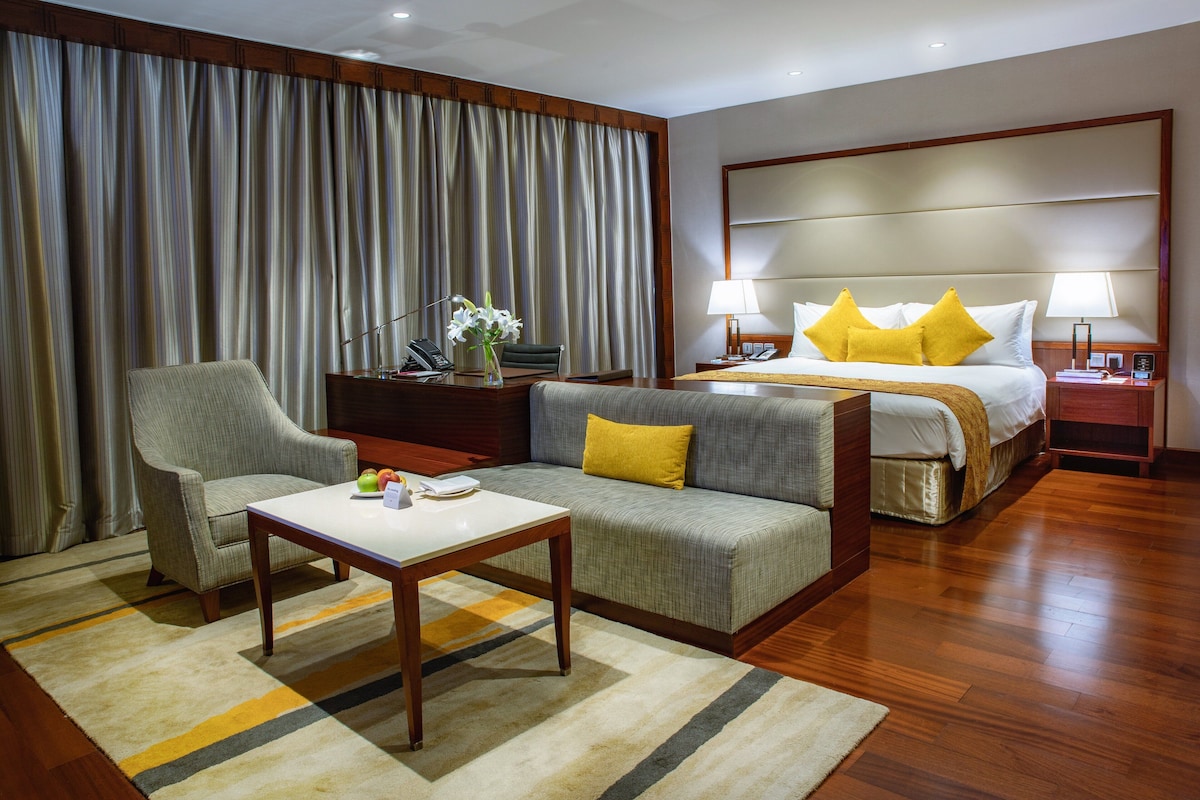 A hotel room with a bed, a sofa, a chair, a table, and a desk with a lamp.