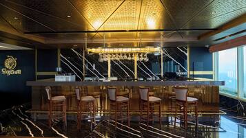 A bar area with a marble floor, bar stools, a bar counter, and a ceiling with a perforated design.