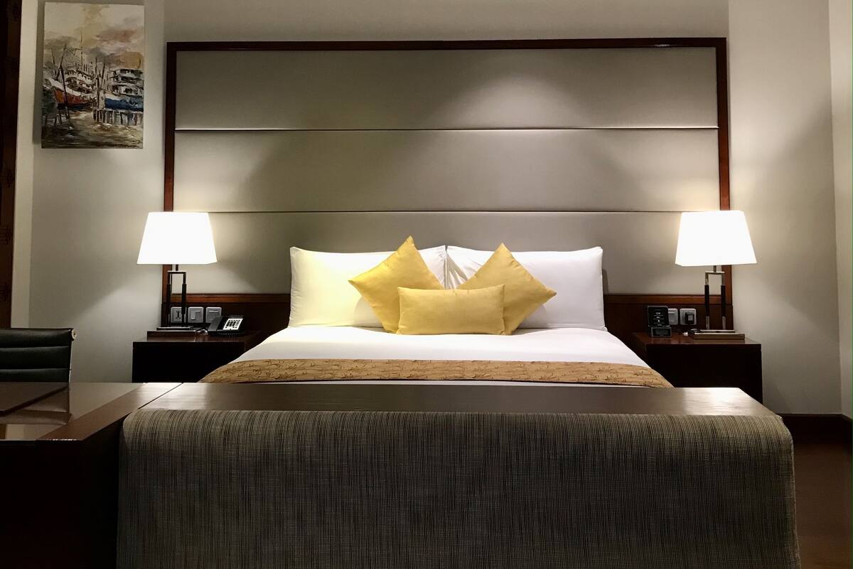 A hotel room with a large bed, two bedside lamps, a nightstand with a phone, and a painting on the wall.