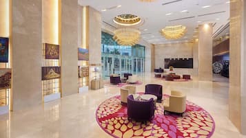 Eine großzügige Lobby mit poliertem Marmorboden, einer zentral gelegenen Sitzecke mit violetten und beigen Stühlen und einer großen Chandelier.