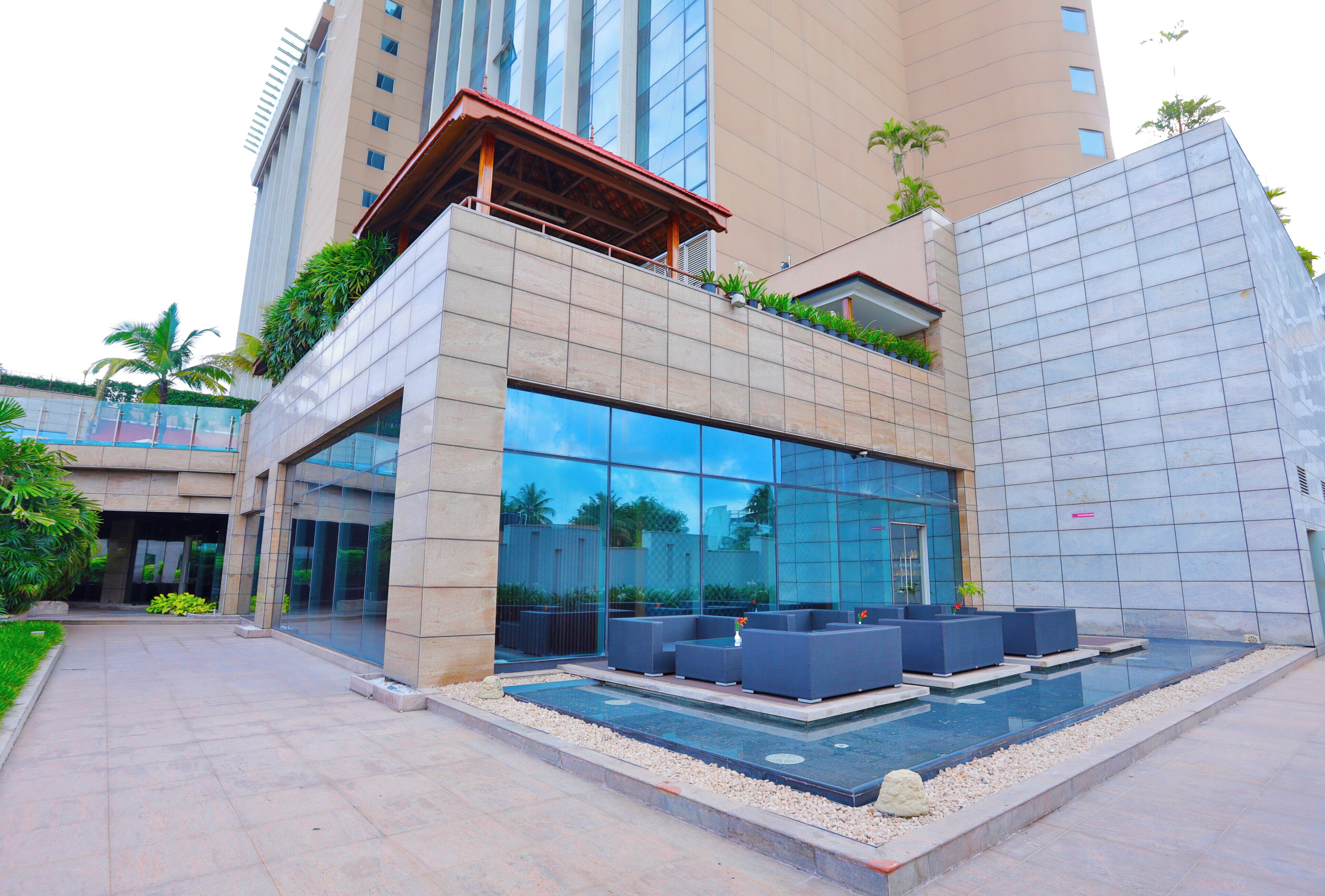 A modern hotel with a glass facade, outdoor seating area, and a pool.