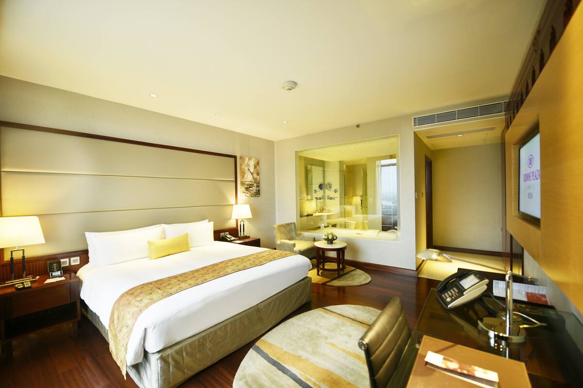 A hotel room with a large bed, bedside tables, a desk, a chair, a mirror, and a television.