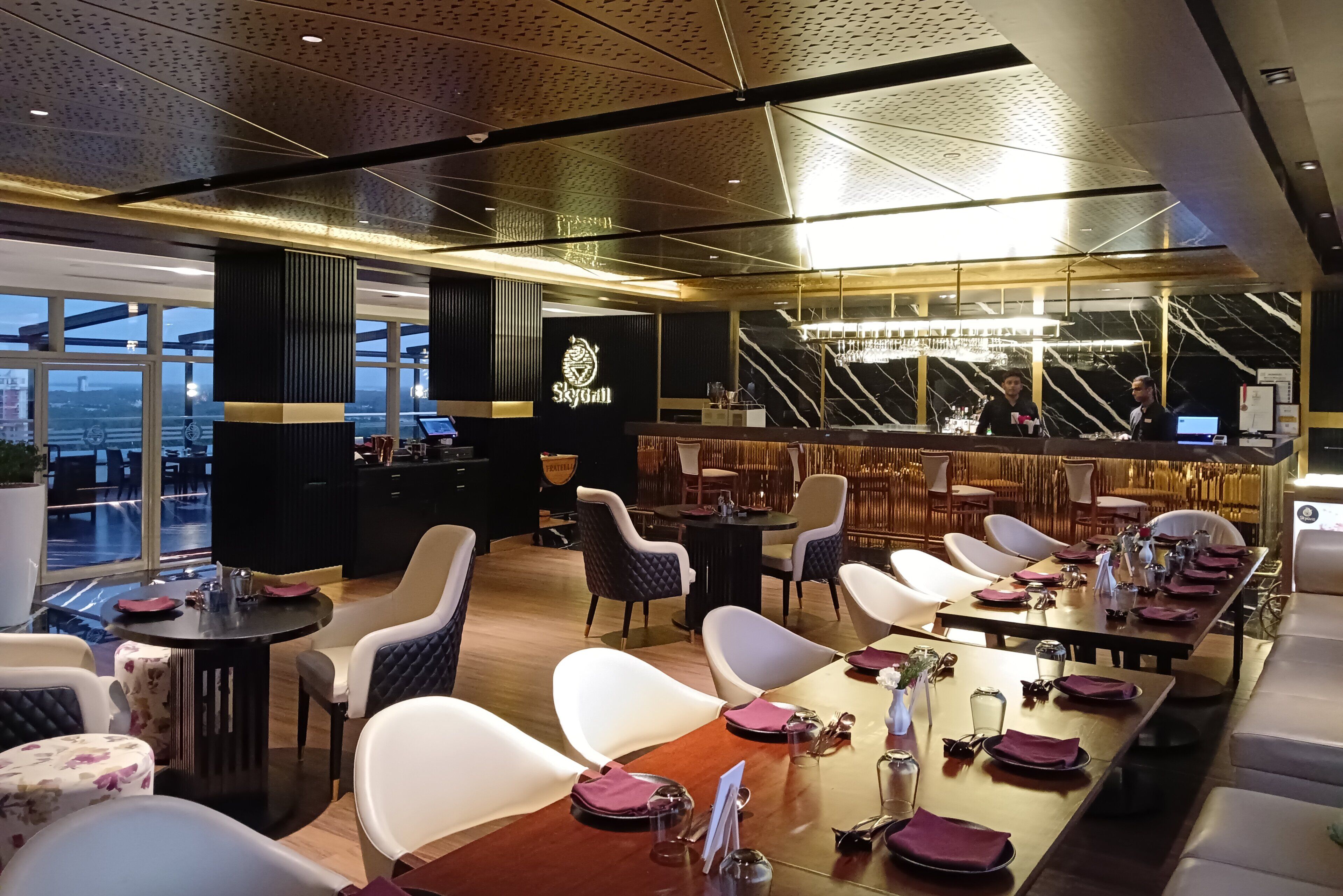 A modern restaurant with a bar area, high ceilings, and a view of the cityscape.