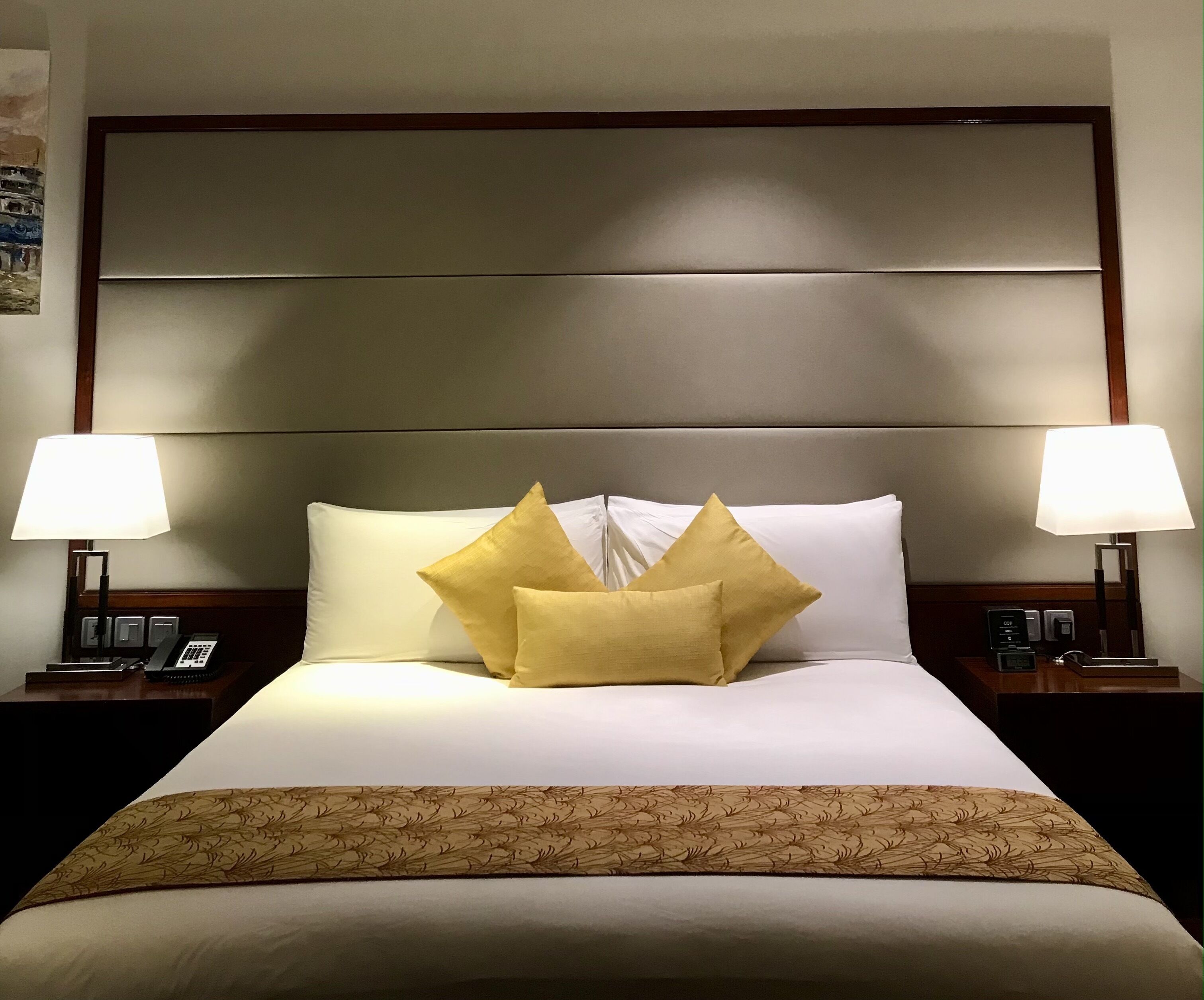 Habitació d'hotel amb un llit gran, dues làmpades de nit, un telèfon i un panell de llit decoratiu.