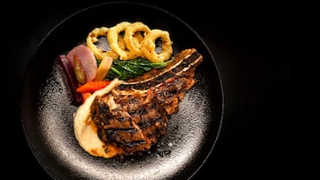 Un bistec acompañado de verduras a la parrilla y aros de cebolla sobre un plato negro.