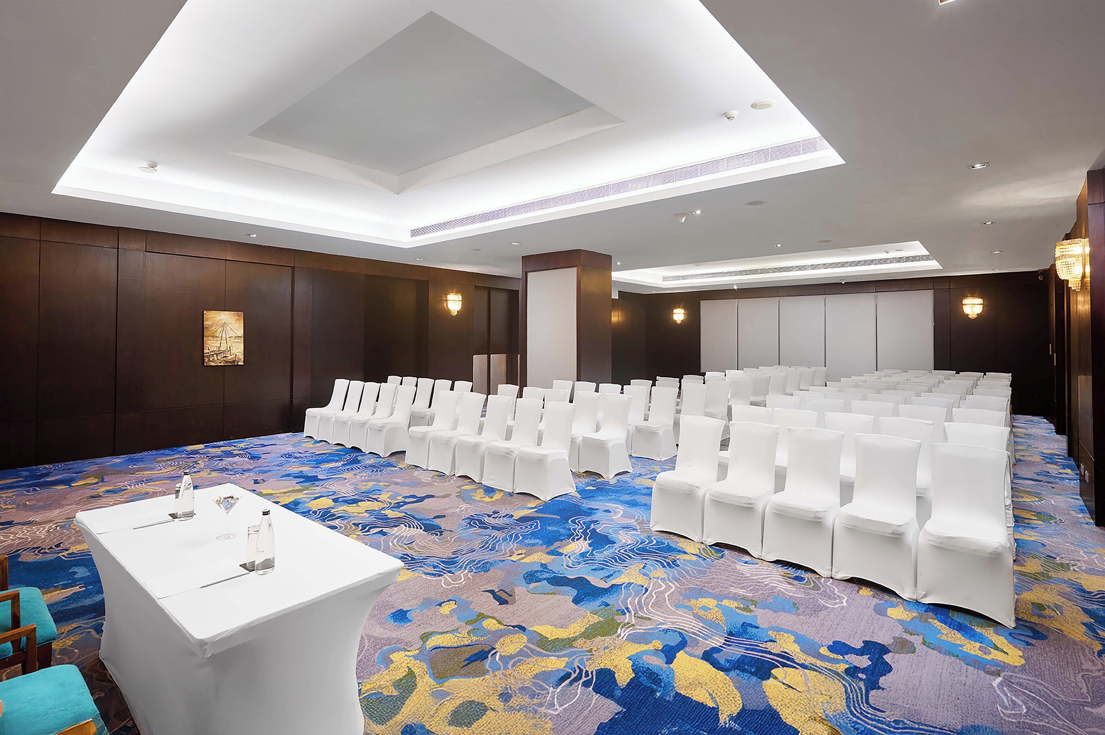 A conference room with white chairs, a white table, and a colorful carpet.